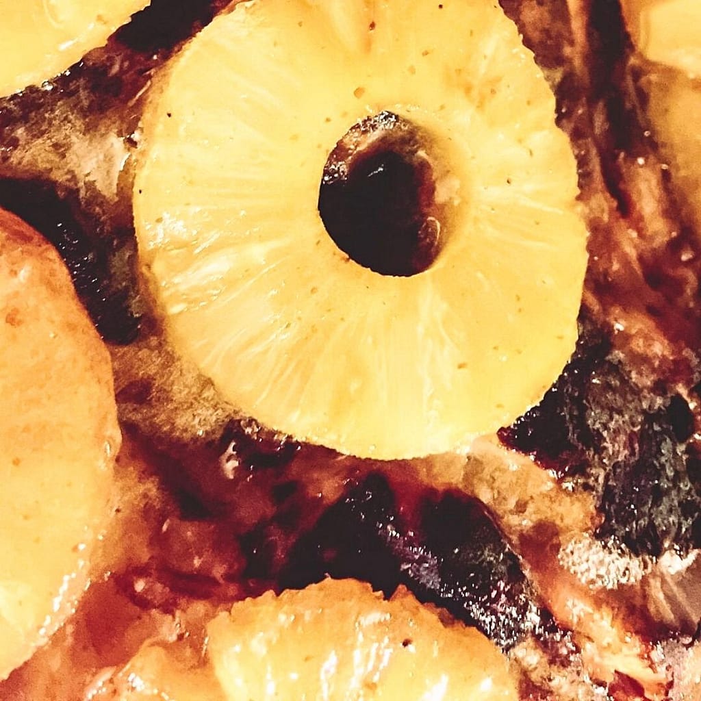 Pineapple rings stuck to the side of cooked, somewhat blackened, ham. It's honey holding it in place.
