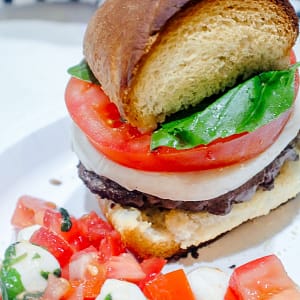 Caprese Burger featuring hamburger topped with tomato, fresh mozzarella, and basil on french bread garlic toast
