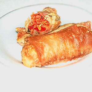Photo of Chicken Empanadilla Egg Rolls on white plate. One is cut in half displaying Puerto Rican Chicken goodness with red peppers and cilantro.