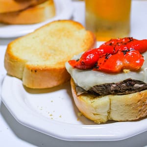Photo of Italian Burger with mozzarella cheese and red pepper on Texas Garlic Toast on a white plate served with an ice cold beer.